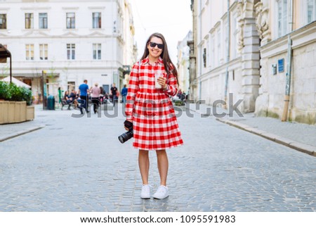 woman walking by city streets with cool drink and camera