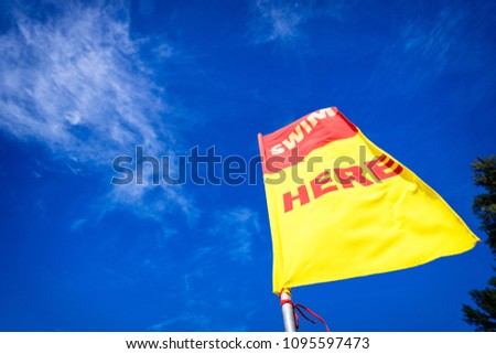Swim here. Safety flag against blu sky on the sea beach.