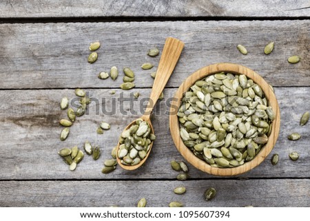 pumpkin seeds in a wooden plate, next to a wooden spoon, on a wooden background, space for text
