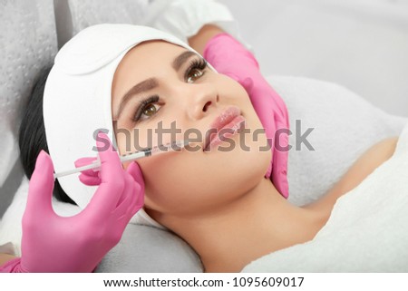 Studio photo of cosmetological lips enlargment process. Medical injection for plump, soft, large lips. Young model with beatiful face wearing white headbandage. Profassional wearing pink gloves.