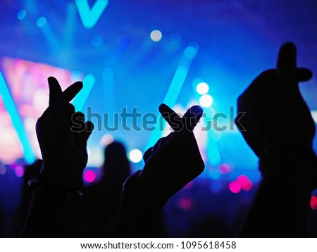 K-Pop music theme or Live concert background with silhouette hands of audience making mini heart shaped hand gesture for artist supporting on blurred background of audience and stage with neon light. Royalty-Free Stock Photo #1095618458