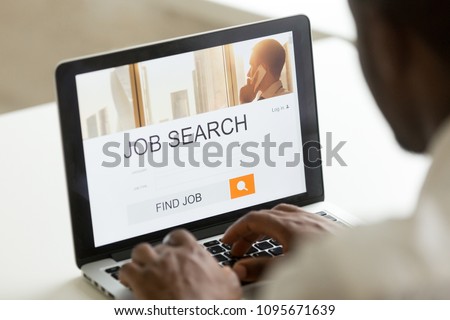 Unemployed worker looking at screen for open job positions online at web page, using work search application, browsing internet. Recruiting, hiring, cv website concept. Close up over the shoulder view