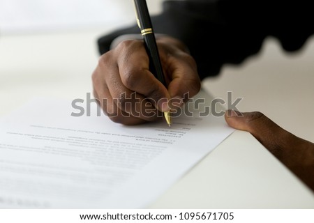 Close up of African American worker signing job contract, person being employed at new position, male client putting signature at document in office. Recruiting, promotion, legal documentation concept