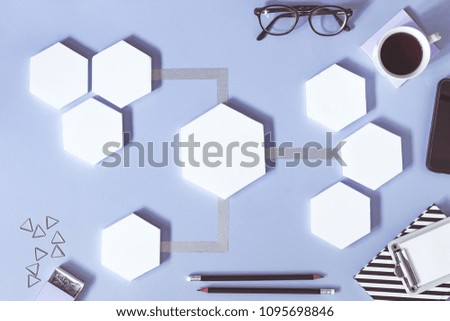 Creative desk with white mock up hexagon shapes of diagram, office accessories, notebooks and cup of coffee. Concept of modern approach to management project. Blue background desk.