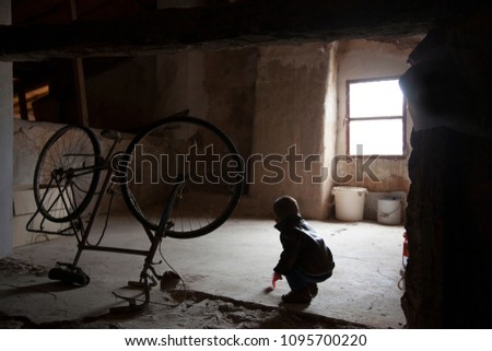 photos of a small child playing in an old, dirty and dark attic where you can see an old broken bicycle, thanks to the light that enters though a window