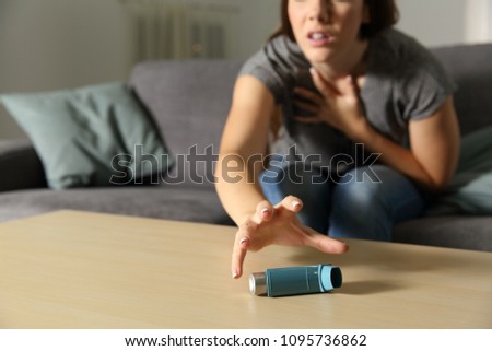 Asmathic girl catching inhaler having an asthma attack sitting on a couch in the living room at home Royalty-Free Stock Photo #1095736862