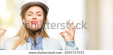 Young woman with bike helmet and earphones doing ok sign gesture with both hands expressing meditation and relaxation