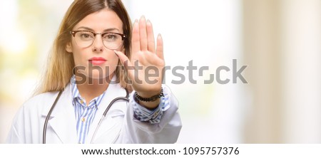 Young doctor woman, medical professional annoyed with bad attitude making stop sign with hand, saying no, expressing security, defense or restriction, maybe pushing