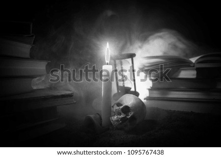 Wizard's Desk. A desk lit by candle light. A human skull, old books on sand surface. Halloween still-life background with a different elements on dark toned foggy background. Selective focus