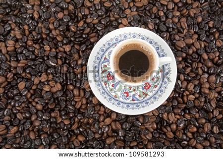 Cup of black coffee on a saucer on roasted coffee beans