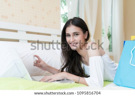 Picture of Asian happy woman doing online shopping  on laptop with credit card in bed at home.

