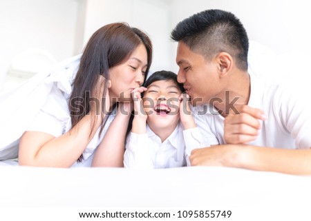 Asian Parents kissing their little son on both cheeks.