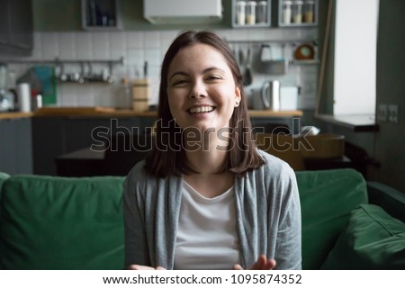 Smiling millennial girl laughing sitting on kitchen sofa talking by videocall looking at camera, female teen video blogger recording vlog at home, casual videoblogging concept, head shot portrait Royalty-Free Stock Photo #1095874352
