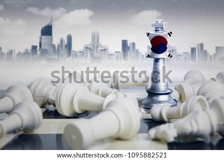 Picture of South Korea flag on a chess king standing near fallen white chess pieces. Shot with modern city