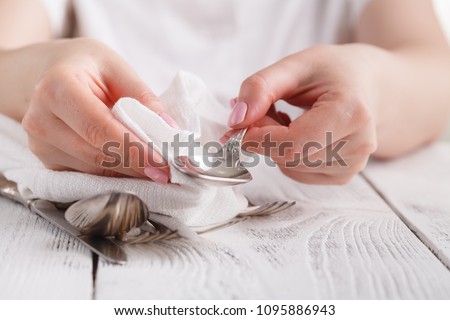 Female hand cleaning spotty silverware with a cleaning product and a cloth,Close up woman hand cleaning silver spoon,polished silver Royalty-Free Stock Photo #1095886943