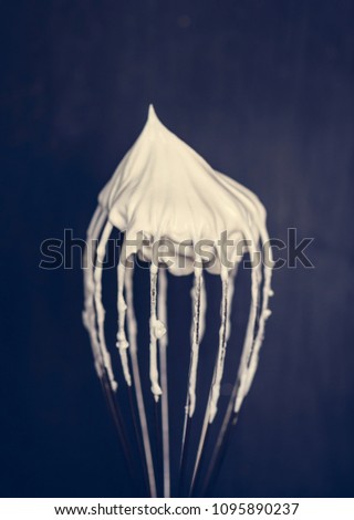 Close up of a wire whisk with whipped cream on top