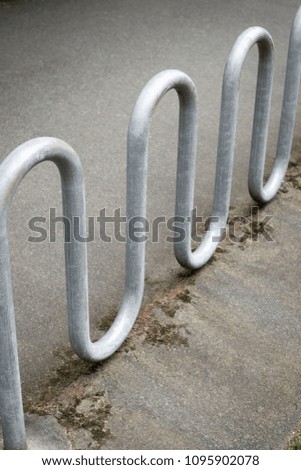 Close up on an empty galvanized steel bike rack beside a path at a park, with space for text on top and bottom