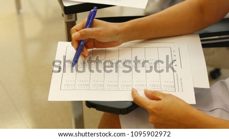 Dark blue pen in right hand and left hand on white paper over lecture chair