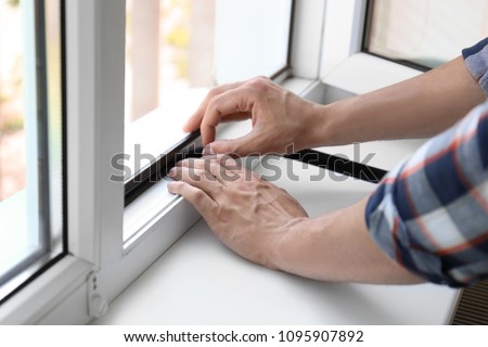 Young man putting sealing foam tape on window indoors Royalty-Free Stock Photo #1095907892