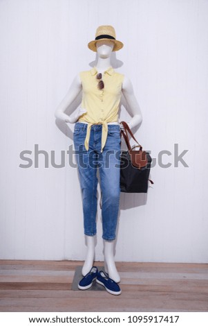 full-length mannequin in female yellow shirt with blue jeans,shoes,hat, handbag –wooden  background
