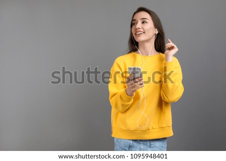 Young woman using phone for listening to music against color background