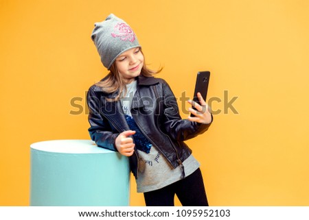 Cute pretty stylish girl in fashionable clothes taking selfie on yellow background.