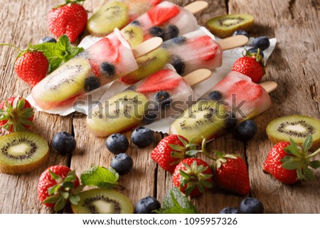 frozen strawberry, kiwi, blueberries water popsicles stick close-up on a table. horizontal
