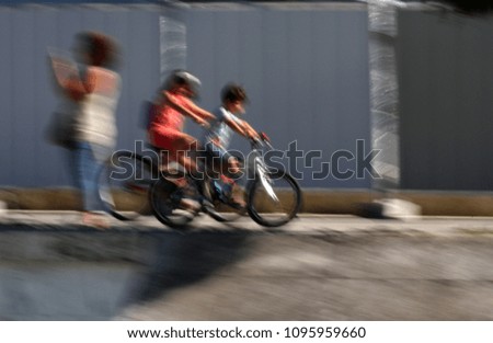 Motion blur picture of children ride bikes. Motion blurred photo with riders. Motion picture of kids ride a bikes in a park background. Blurred wallpaper with people do sports.