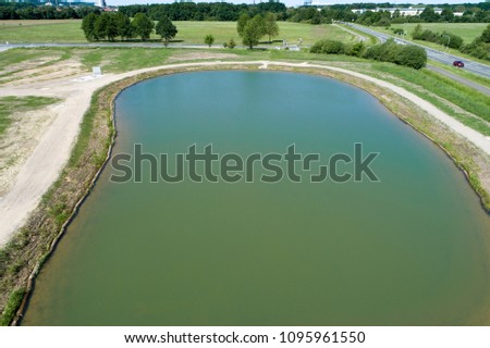 Rainwater retention basin with turquoise coloured water, taken diagonally from the air with a drone, Germany
