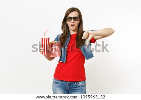 Portrait of young dissatisfied woman in 3d glasses watching movie film, holding bucket of popcorn and plastic cup of soda or cola, showing thumb down isolated on white background. Emotions in cinema