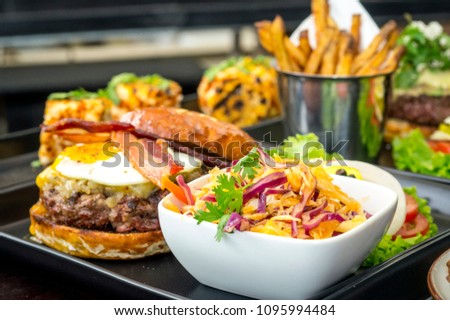 A delicious hamburger topped with onion, fried egg, bacon. Salad vegetable 
