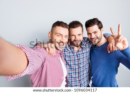 Self portrait of cheerful, positive, cool, stunning, virile, modern guys shooting selfie on smart phone, embracing, gesturing v-sign, isolated on grey background