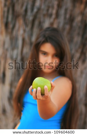 A portrait of a little girl holding a green apple (focus on the apple), vertical picture