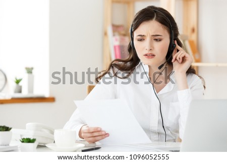 Serious well-dressed saleswoman talking on phone in office behind her desk and laptop computer. Copy space