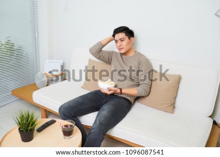 Bored asian man watching tv on the couch at home in living room