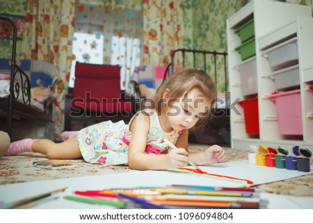 Little girl lies on bedroom floor and paint picture