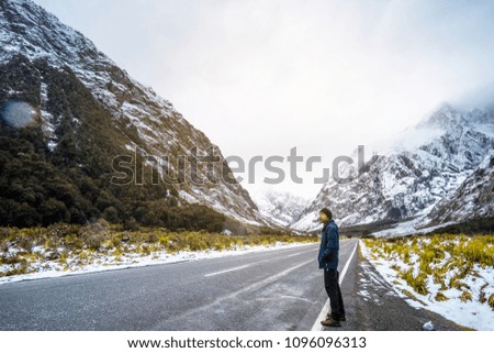 A young Asian man standing on the road among snow mountain.