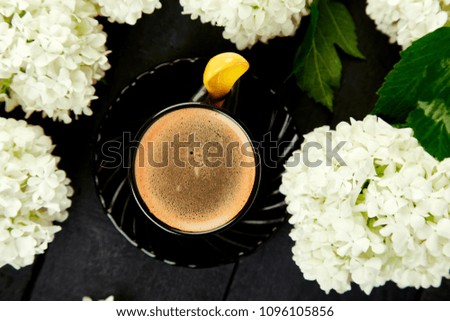 Cup of coffee with bouquet flower hydrangea on black wooden background. Good morning. Flat lay. Top view.