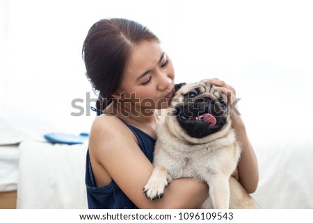 Beautiful Asian young woman playing with her pet and smile with pug dog looking in funny face in bedroom