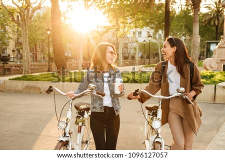Picture of two young happy women friends outdoors with bicycles in park.
