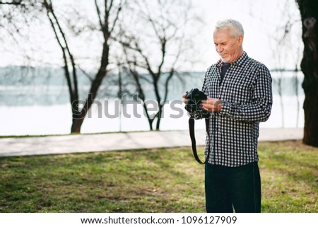 Create image. Jolly senior man staring down and using camera