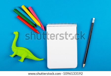 Notebook next to colored pencils and a children's doll on blue background. Back to school concept.
