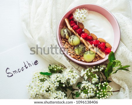 Healthy food. Berry smoothie, muesli with nuts, dry berries, pieces of banana and kiwi in a pink plate, branch of beautiful, blooming flowers, notebook with an inscription on a stylish table. Top view
