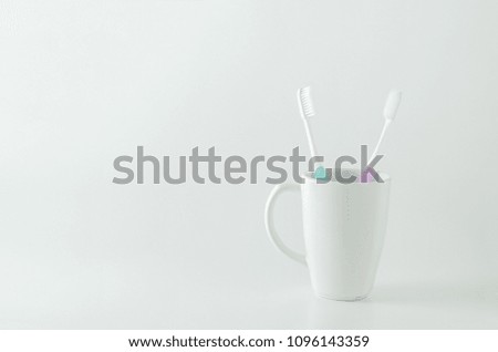 Green and purple toothbrush with white ceramic mug on white background