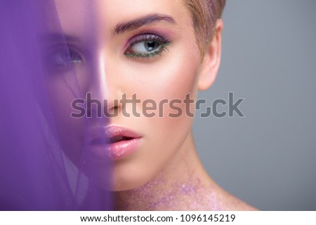 attractive woman with violet glitter on neck looking away isolated on grey