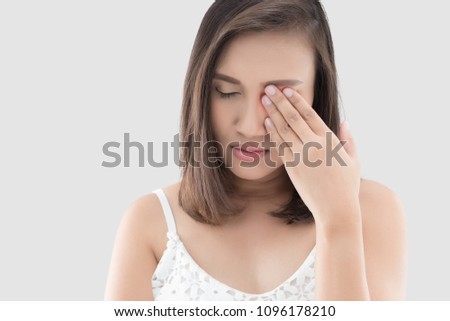 Asian woman suffering from strong eye pain against a gray background. Female has a pain in the eye. Healthcare concept. Having migraine Royalty-Free Stock Photo #1096178210