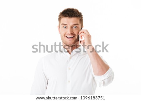 Portrait of an excited young man talking on mobile phone isolated over white background