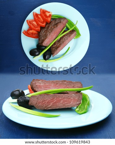 meat savory : grilled beef fillet mignon on blue plate with pepper chives and black greek olives over blue wooden table