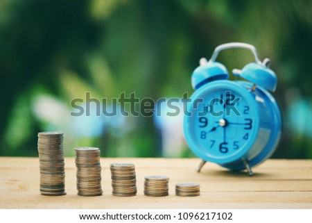 close up stack of coin and blue alarm clock on old wood table, green nature copy space background for text, saving money for future, manage time for success business concept