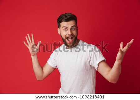 Picture of excited young handsome man standing isolated over red wall background. Looking camera.